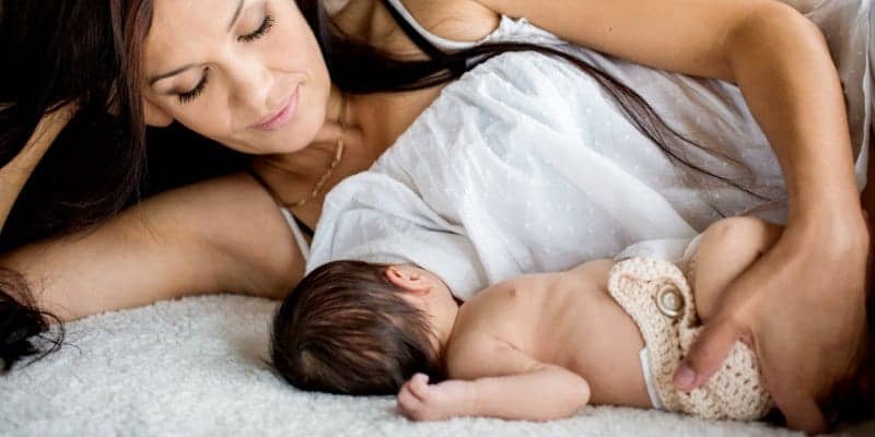 mother breastfeeding and nursing baby lying down on bed 