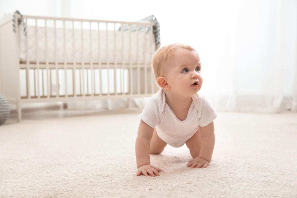 5 month old baby crawling on white carpet in a white onesie