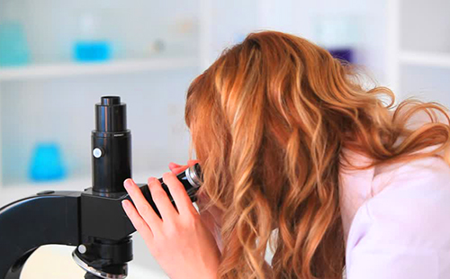 Рыжая девушка смотрит в микроскоп