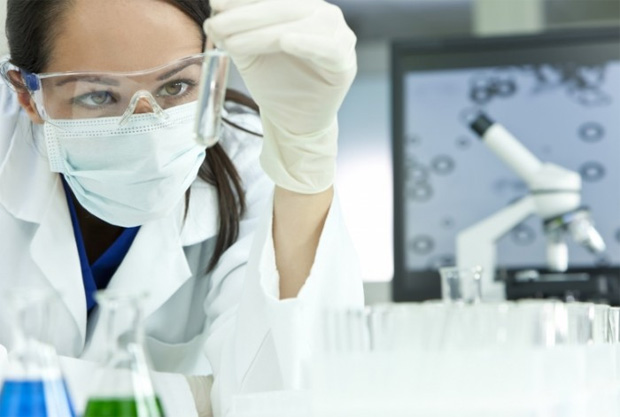 Молодая девушка в защитных маске и очках проводит исследования в лаборатории