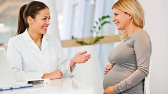 A photo of a pregnant woman talking with her doctor.
